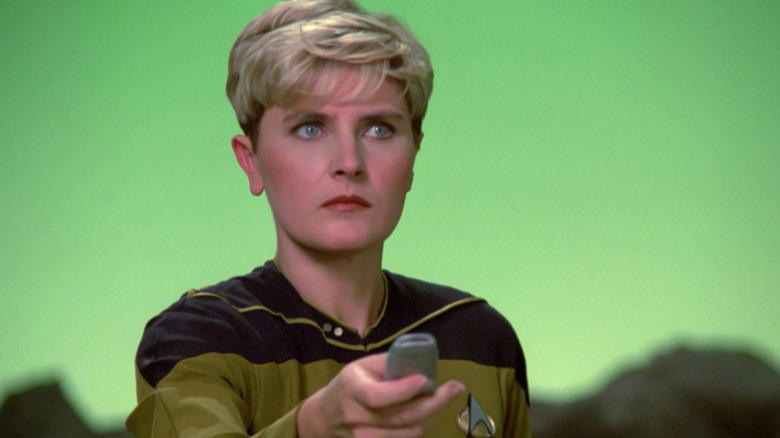 Denise Crosby dans le rôle de Tasha Yar tenant un appareil portable et debout devant un fond vert dans Star Trek : la nouvelle génération