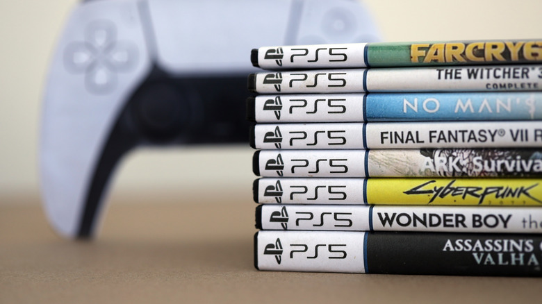 Une pile de boîtes de disques de jeu PS5 avec une manette en arrière-plan