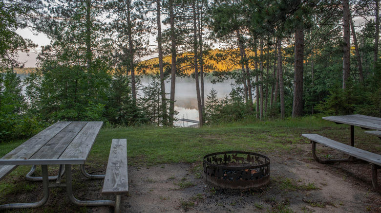 Tables de pique-nique et foyer donnant sur un lac à travers les arbres