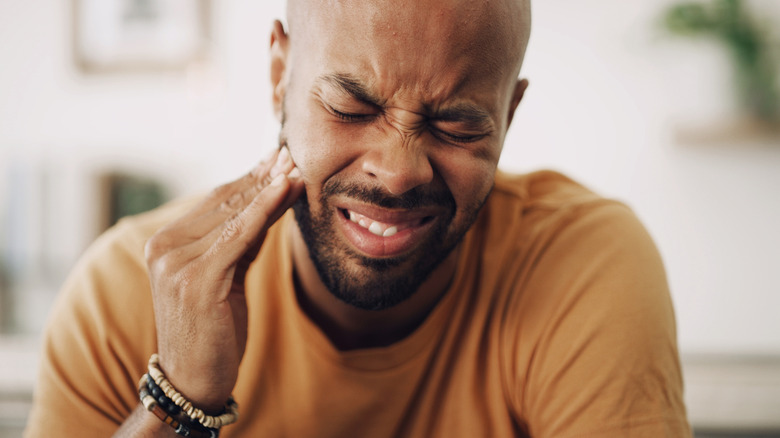Homme touchant le côté du visage à cause d’une douleur dentaire
