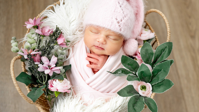 Une petite fille dormant dans un panier de fleurs