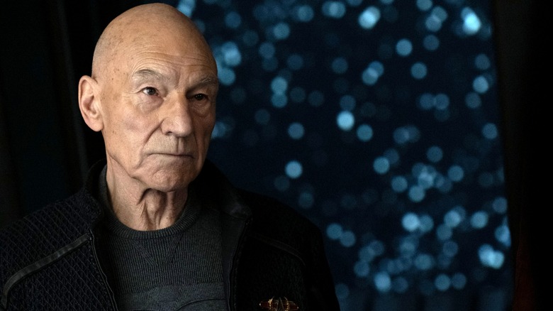 Patrick Stewart dans le rôle de Jean-Luc Picard debout près d'une fenêtre affichant un champ d'étoiles dans Star Trek : Picard