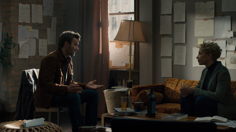 Joel Edgerton dans le rôle de Jason Dessen assis dans une pièce couverte de notes de recherche en face d'Amanda Brugel dans le rôle de Blair Caplan dans Dark Matter